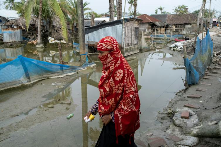 A woman in a red headscarf walks along a flooded road.